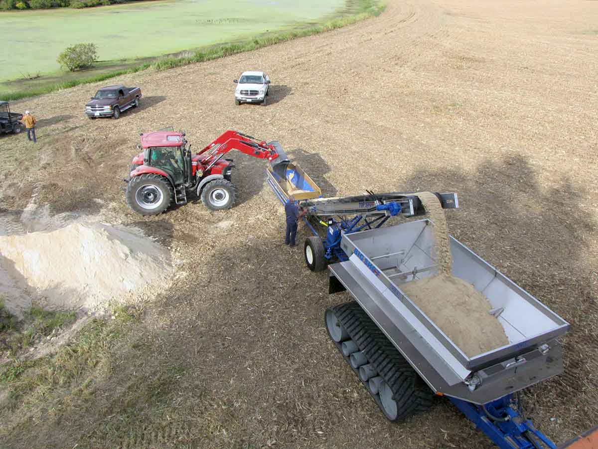 Top Shot Aggregate Conveyor loading Lime into a doyle spreader in a field
